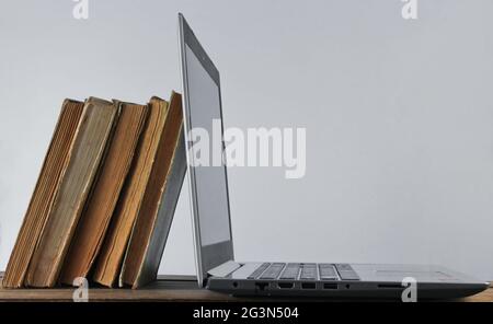 Modern laptop and stack old books  on wooden shelf against the white wall background. Old and new sources of information. Stock Photo