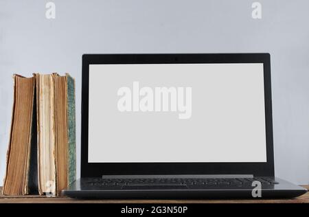 Modern laptop and stack old books  on wooden shelf against the white wall background. Old and new sources of information. Stock Photo