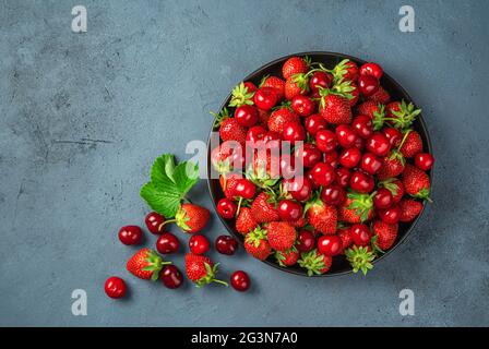 Fresh summer fruits and berries on a dark background. Juicy cherries and strawberries in a black plate. Stock Photo