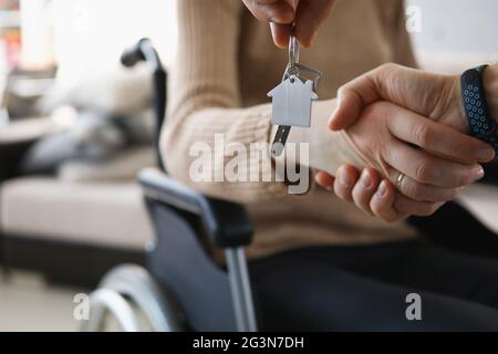 Disabled woman in wheelchair shaking hands with man with keys to new apartment closeup Stock Photo