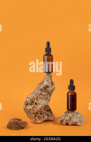 Serum or essential oil in brown glass dropper bottle on stones, orange background. Natural Organic Spa Cosmetic concept Front view. Stock Photo