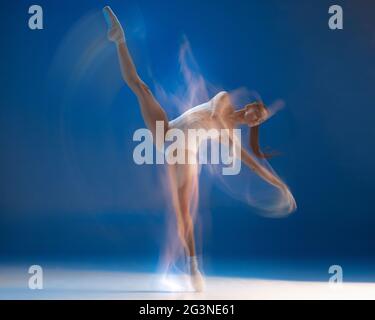 On the tips of toes. Young beautiful ballerina in action isolated over blue background. Stock Photo