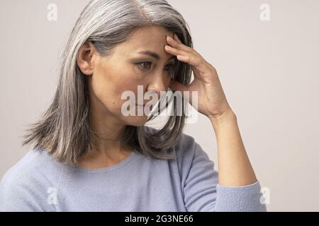 Mature Asian woman touches her forehead in distress Stock Photo