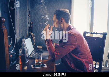 Handsome man works on his laptop smoking and drinking Stock Photo