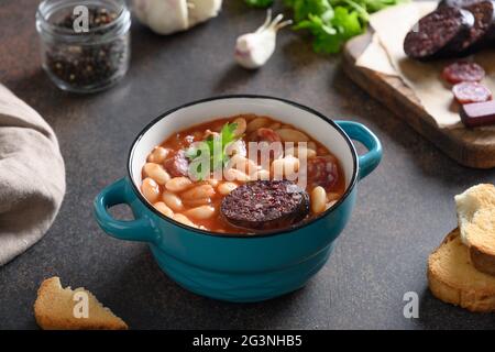 Asturiana traditional stew fabada with haricot, tomatoes, blood sausage on brown table. Close up. Stock Photo