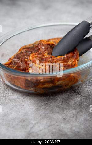 Lamb chops with a mint sauce marinade in a glass dish with kitchen tongs.  On a concrete background Stock Photo