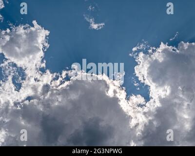 Sunrays shining through white clouds on blue sky background Stock Photo