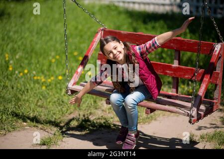Smiling Little Girl With Long Pigtails Is On The Swing In The Park. Stock Photo