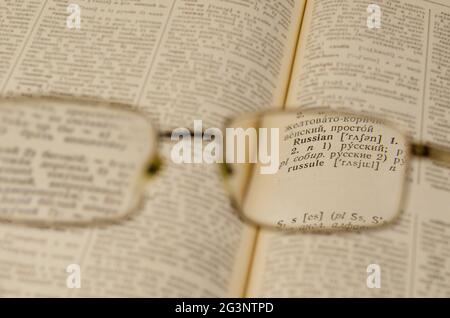 Reading glasses and an open book in close-up. Old Russian-English Dictionary. Selective Focus on the word RUSSIAN. Stock Photo