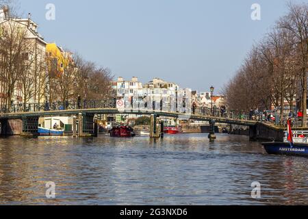 Amsterdam, Netherlands -12 March 2016: Bridge pedestrians and cyclists over the Amstel canal. Typical dutch houses. Stock Photo