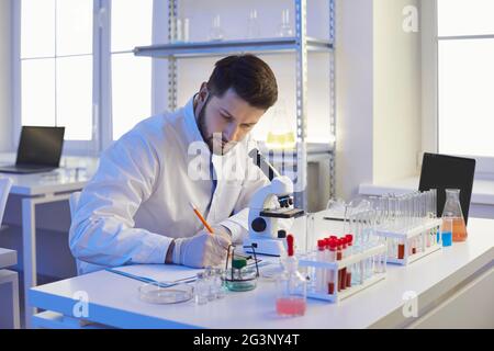 Scientist taking notes sitting at a table in a pharma or microbiology laboratory Stock Photo