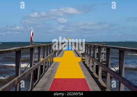 A jetty with a colourful carpet in blue, yellow and red. A blue ocean and sky in the background. Picture from Scania county, Sweden Stock Photo