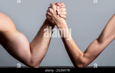 Arm wrestling. Heavily muscled man arm wrestling a puny weak man. Arm wrestling thin hand and a big strong arm in studio. Two man's hands clasped arm