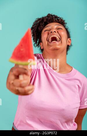 Black girl eating a slice of watermelon in the form of ice cream on a turquoise background Stock Photo