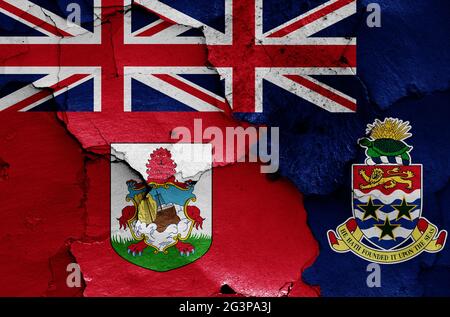 flags of Bermuda and Cayman Islands painted on cracked wall Stock Photo