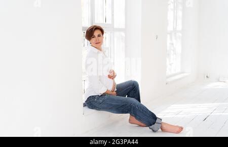 Happy Pregnant Woman Sitting In White Room Stock Photo