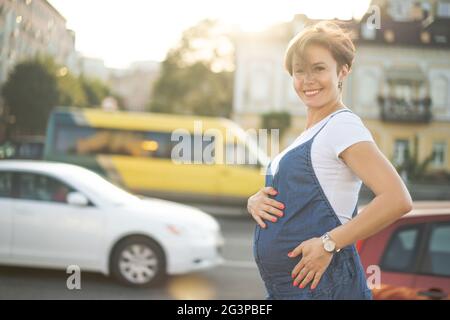 Pregnant Woman Walks Outdoors Through Urban Street In Sunny Day Stock Photo