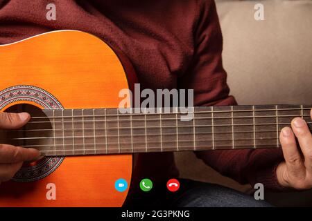 Man giving acoustic guitar lessons while on a video call. Stock Photo