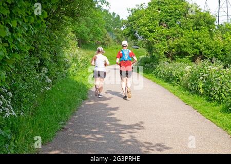 Two older people couple rear back view runners running jogging along Walthamstow Wetlands path in spring countryside 2021 London N17 UK KATHY DEWITT Stock Photo