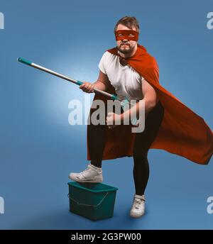 Superhero ready for cleaning work. Man in a mask and superhero red cloak posing with a bucket and a mop presenting himself as a Stock Photo