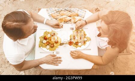 High angle view couple in love sitting at a table on a sandy beach Stock Photo