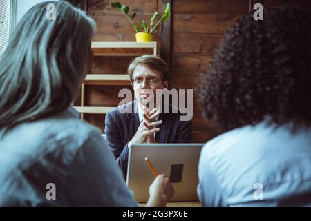 Brainstorming of Multi ethnic team. Focus on smart caucasian man sitting at negotiating table with grey-haired woman and woman w Stock Photo