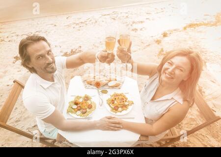 Romantic couple drink wine at seaside cafe outdoors. Happy middle aged man and woman have date near the sea. High angle view. To Stock Photo