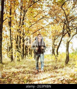 Traveler backpacker walking in autumn forest, young caucasian man in gray jacket goes along the trail admiring beauty of nature