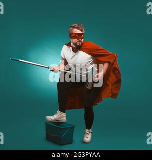 Superhero rock musician is cleaning. Man wearing a red cloak and mask holds a mop representing himself a musician putting his fo Stock Photo