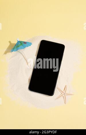 Sand island with smartphone, umbrella and starfish on yellow background, summer concept, mock-up, close up. Stock Photo