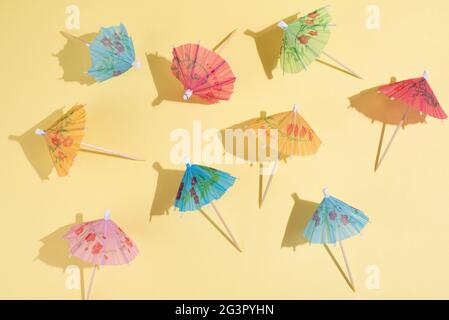 Multicolored cocktail umbrellas on yellow background in bright sunlight, summer party background, close up. Stock Photo