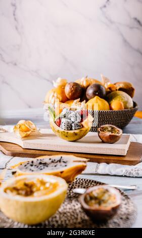 Bright food photography of mix of sliced tropical fruits. Backdrop with a tray with passion fruit, maracuya, physalis, orange, dragon fruit and raspbe Stock Photo
