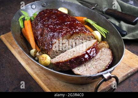 Traditional American meatloaf with ketchup from ground beef with carrots and onion as closeup in a copper saucepan