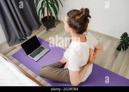 Healthy young female meditating at home watching online tv yoga class e tutorial on laptop doing virtual pilates exercises, relaxing body and mind, me Stock Photo