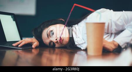 Bored office girl relaxing at workplace. Crazy business woman drinks coffee lying on the table. Crisis concept. Tinted image Stock Photo