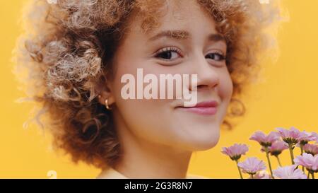 Beautiful girl with curly hair holding a bunch of purple flowers. Girl smiling and in a good mood wearing earrings. Isolated over bright yellow background studio. High-quality photo  Stock Photo