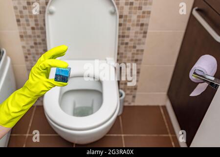 Toilet cubes cleaner in hand. A hand lowers a disinfectant cube into the water of a toilet bowl built into the wall Stock Photo