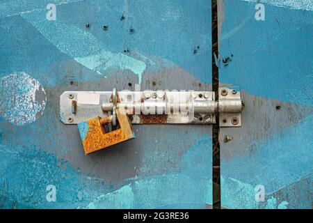 Rusty padlock attached to bolt on blue painted door Stock Photo