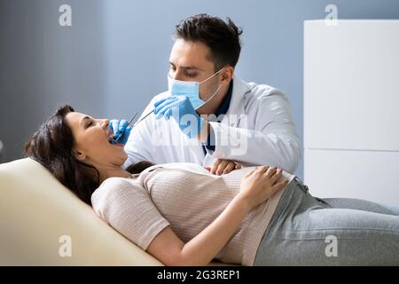 Dentist Treating Teeth Of Young Pregnant Woman Patient Lying In Clinic Stock Photo