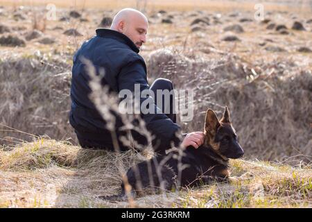 Owner petting young German Shepherd dog that sits beside him Stock Photo