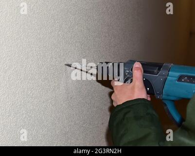 A drill with a drill drills a hole in a concrete wall Stock Photo