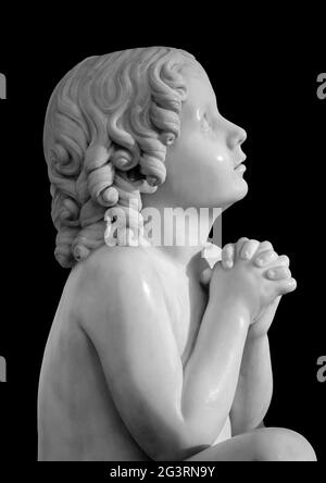 Boy statue pray to God with hands held together. Beautiful old stone statue of praying child isolated on black background Stock Photo