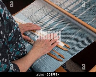 Artisan's hands with two shuttles on the hand loom. Weaving of the fabric with striped pattern Stock Photo