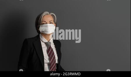 Serious gray haired businesswoman wearing protective mask and formalvear isolated on gray background. Copy space at right Stock Photo
