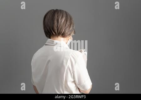 Rear view of female doctor in white coat using digital tablet standing back on gray background. Copy space Stock Photo