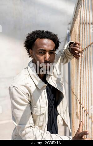 Afro man leaning on metallic fence while looking at camera Stock Photo