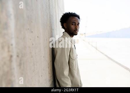 Black man leaning on concrete wall with hands on pocket Stock Photo