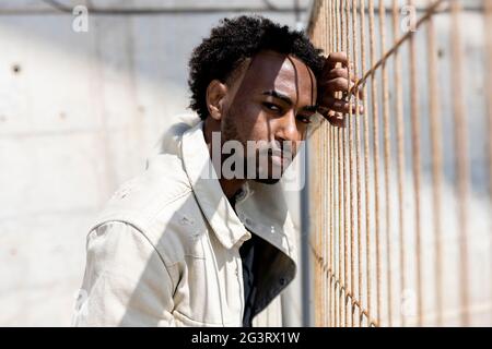 Afro man leaning on metallic fence while looking at camera Stock Photo
