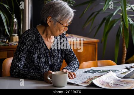 Senior woman reading newspaper while sitting at table with coffee Stock Photo