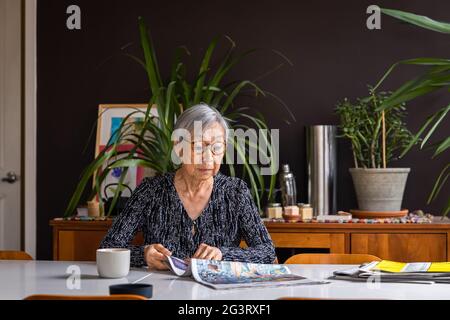 Senior woman reading newspaper while sitting at table with coffee Stock Photo